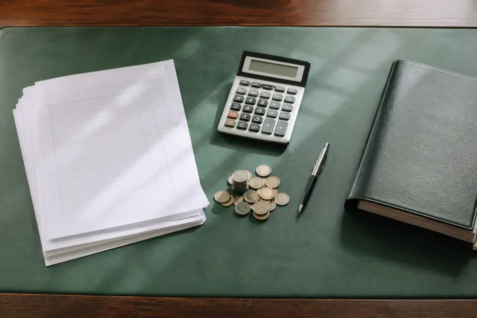 Calculator, paperwork, coins and a tabbed binder on a green desk mat