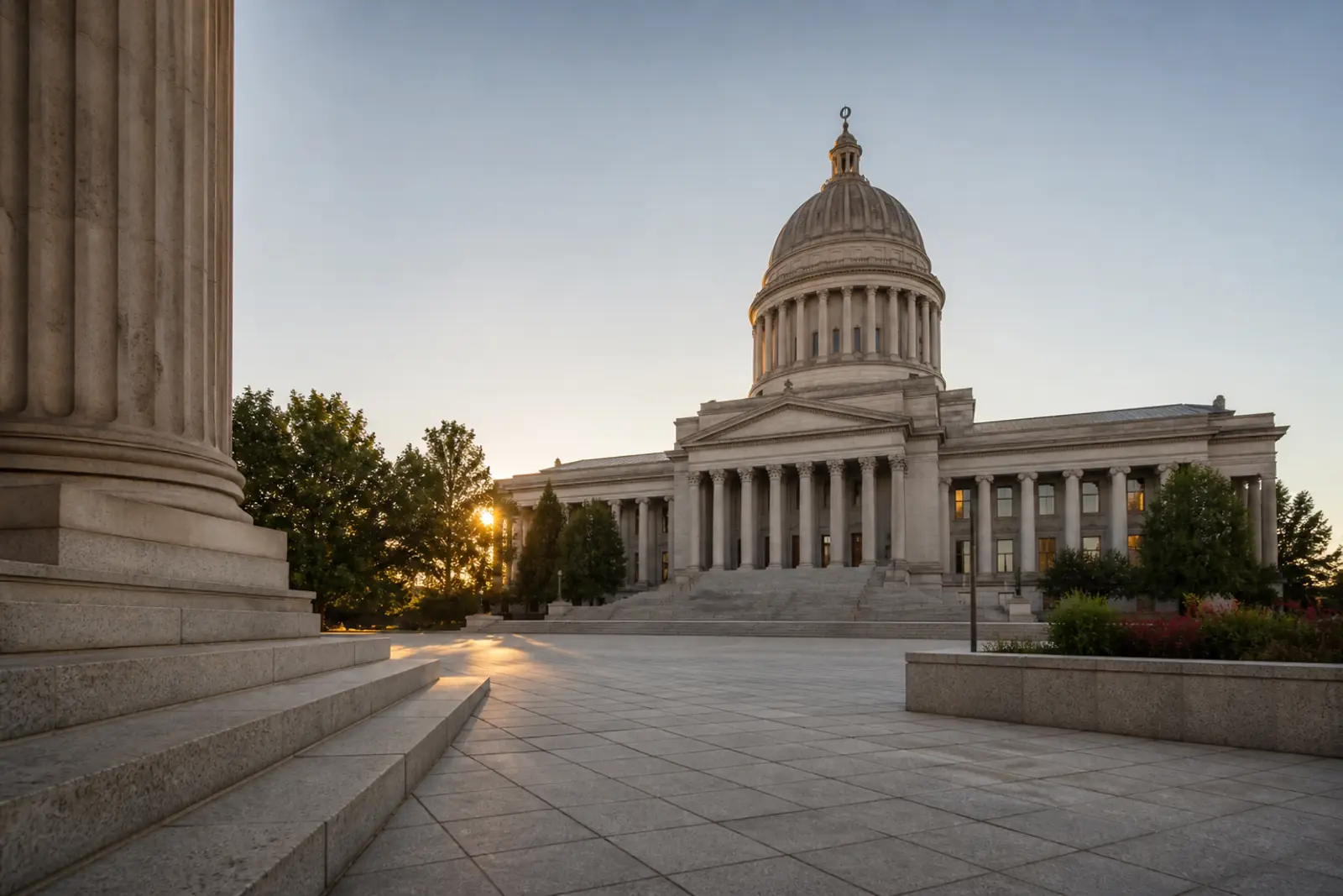A state capitol building at dawn seen from a quiet plaza, soft early light on stone steps, no flags with text, no seals, no people